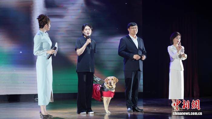 Eine Verantwortliche fuer Aussenkontakte der Blindenfuehrhund-Ausbildungsbasis Dalian in China erscheint mit einem Blindenfuehrhund bei einer Themenveranstaltung zum Tag der Behindertenhilfe. Bildquelle: Nachdruckseite von China News Service.